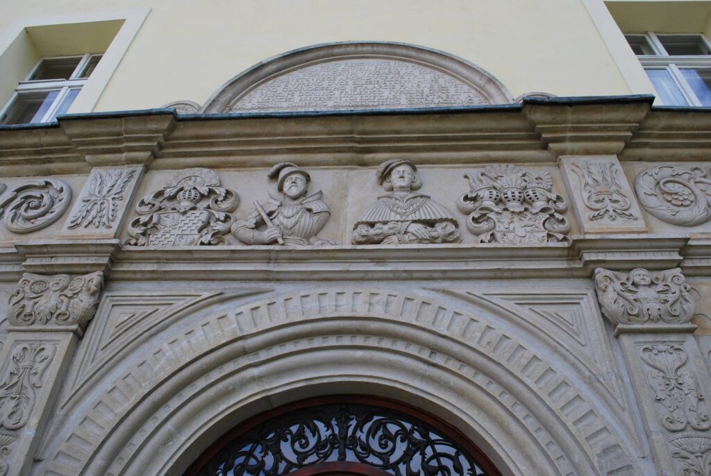 Chojnów. Zamek książąt legnicko-brzeskich. Skrzydło południowo-zachodnie rezydencji renesansowej projektu Franciszka Parra, z założeniem portalowym z lat 1546-47 (Faza V). <sup class="modern-footnotes-footnote modern-footnotes-footnote--expands-on-desktop " data-mfn="1" data-mfn-post-scope="00000000000001640000000000000000_9033"><a href="javascript:void(0)"  title="W środkowej partii portalu widoczne popiersia właścicieli – pary książęcej Fryderyka III legnickiego (po lewej) i jego żony Katarzyny von Mecklenburg-Schwerin (po prawej), flankowane przez ich tarcze herbowe. Nad wejściem w półkolistym frontonie znajduje się łaciński napis: „DIVO RENGNANTE FER DINANDO DIVIHA FAVEITE GRA TIA ROMANORVM VAGARIE AC BOM KIMIK ETC RECE ARCHID VCE AVSTRIE NEC MON SVPREMO DVGE SILESIE ECT PRINCIPE NO STRO GLORISISSIMO ISTA ARCIS PARS AB ILLVST RI PRINCIPE DOMINO FRIDERICO IVHIORE DVCE SILE OIE LEGNICESI BREGENSI ETC EDIFACARI INCEPT A EST AN NO DOMINI MILLESIMO GVINGVETISSIMO QVADEAGESIMMO SE A TO ET VICISSIM ANNO DOMINI MILLESIMO QWINGENTE SINO QVADRAGESIMO SEPTIMO” („Za panowania szlachetnego Ferdynanda, z łaski bożej króla Rzymian, Węgrów i Czechów etc., arcyksięcia austriackiego i najwyższego księcia Śląska, naszego najsławniejszego władcy, została ta część zamku przez Jaśnie Oświeconego Księcia Pana Fryderyka Młodszego, księcia śląskiego na Legnicy, Brzegu etc., przebudowana w Roku Pańskim 1546 oraz powtórnie w Roku Pańskim 1547.” / tłum. B. Steinborn 1971),"  role="button" aria-pressed="false" aria-describedby="mfn-content-00000000000001640000000000000000_9033-1">1</a></sup><span id="mfn-content-00000000000001640000000000000000_9033-1" role="tooltip" class="modern-footnotes-footnote__note" tabindex="0" data-mfn="1">W środkowej partii portalu widoczne popiersia właścicieli – pary książęcej Fryderyka III legnickiego (po lewej) i jego żony Katarzyny von Mecklenburg-Schwerin (po prawej), flankowane przez ich tarcze herbowe. Nad wejściem w półkolistym frontonie znajduje się łaciński napis: „DIVO RENGNANTE FER DINANDO DIVIHA FAVEITE GRA TIA ROMANORVM VAGARIE AC BOM KIMIK ETC RECE ARCHID VCE AVSTRIE NEC MON SVPREMO DVGE SILESIE ECT PRINCIPE NO STRO GLORISISSIMO ISTA ARCIS PARS AB ILLVST RI PRINCIPE DOMINO FRIDERICO IVHIORE DVCE SILE OIE LEGNICESI BREGENSI ETC EDIFACARI INCEPT A EST AN NO DOMINI MILLESIMO GVINGVETISSIMO QVADEAGESIMMO SE A TO ET VICISSIM ANNO DOMINI MILLESIMO QWINGENTE SINO QVADRAGESIMO SEPTIMO” („Za panowania szlachetnego Ferdynanda, z łaski bożej króla Rzymian, Węgrów i Czechów etc., arcyksięcia austriackiego i najwyższego księcia Śląska, naszego najsławniejszego władcy, została ta część zamku przez Jaśnie Oświeconego Księcia Pana Fryderyka Młodszego, księcia śląskiego na Legnicy, Brzegu etc., przebudowana w Roku Pańskim 1546 oraz powtórnie w Roku Pańskim 1547.” / tłum. B. Steinborn 1971),</span> 2016 (fot. R. Mruczek, Katalog Zamków i Dworów Obronnych Śląska [https://zamki.pwr.edu.pl/]. Licencja: CC BY-NC 4.0 [https://creativecommons.org/licenses/by-nc/4.0/])